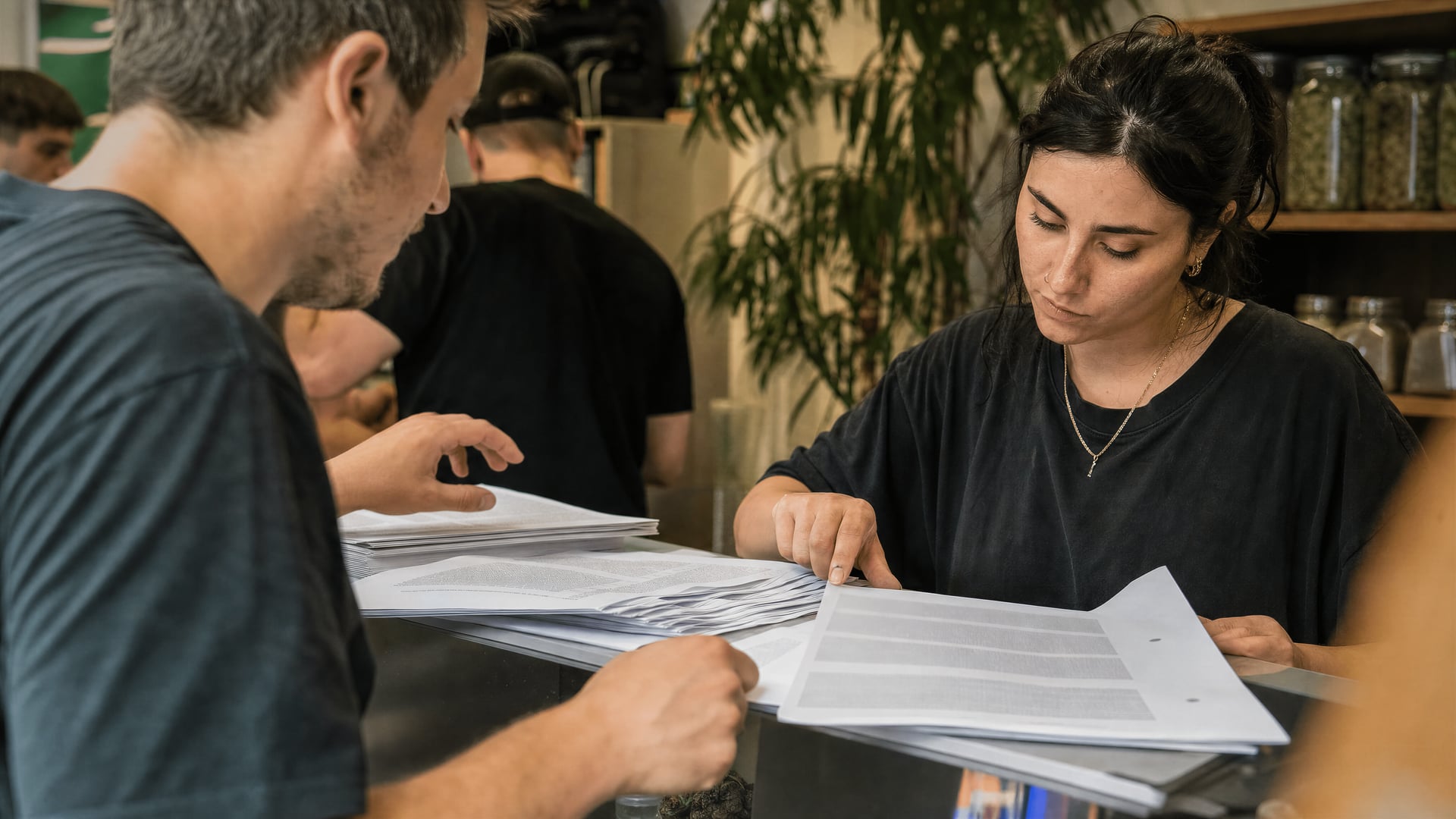 People at a cannabis social club reception desk with legal documents and registration forms.