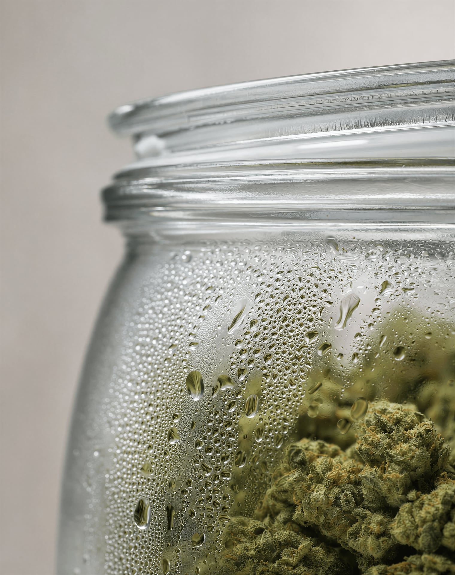 Close-up of moisture droplets inside a cold cannabis jar with flower blurred behind the glass.