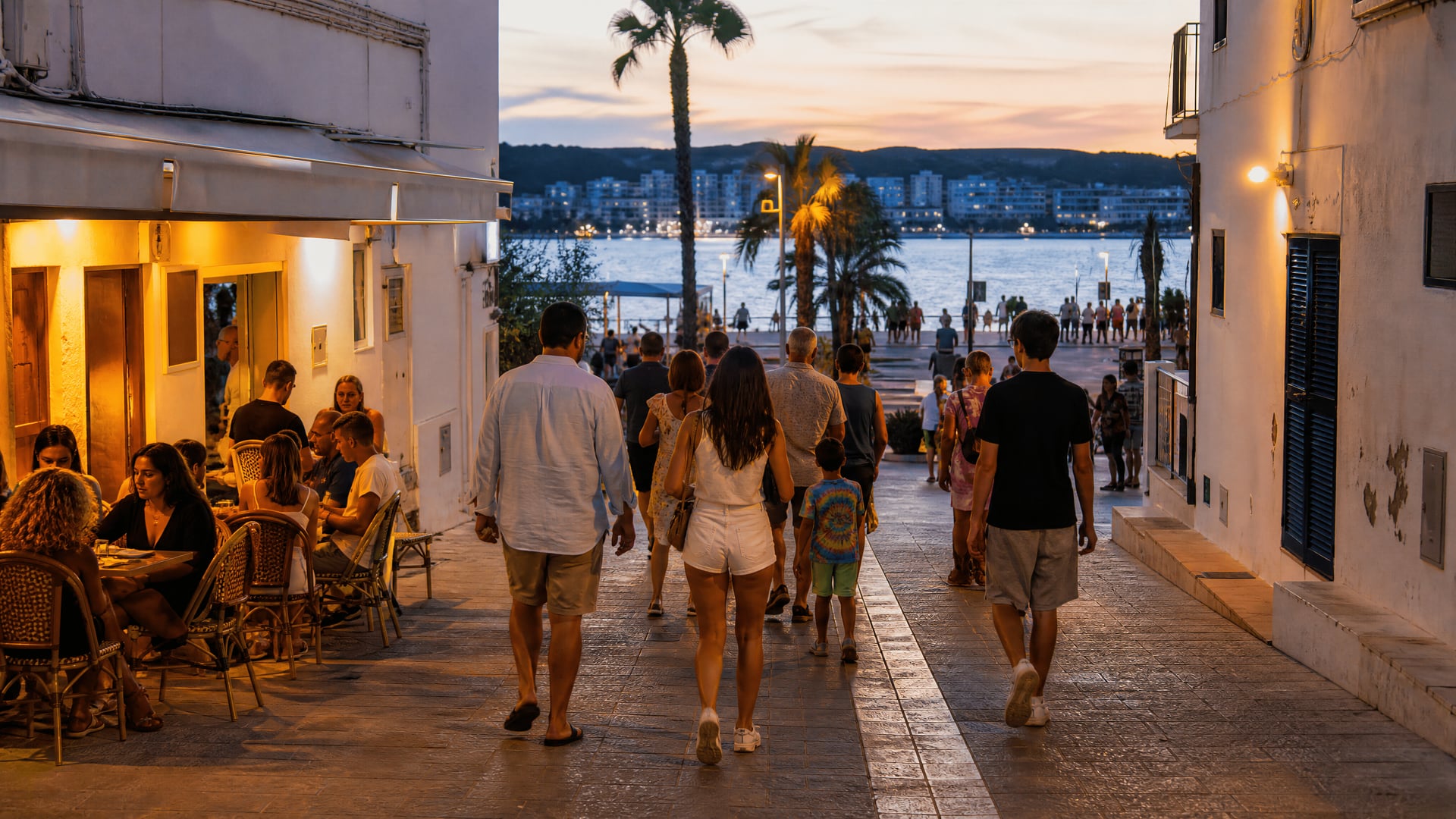 Rua lateral ao anoitecer em Sant Antoni de Portmany com pessoas a caminhar em direção ao passeio e cafés
