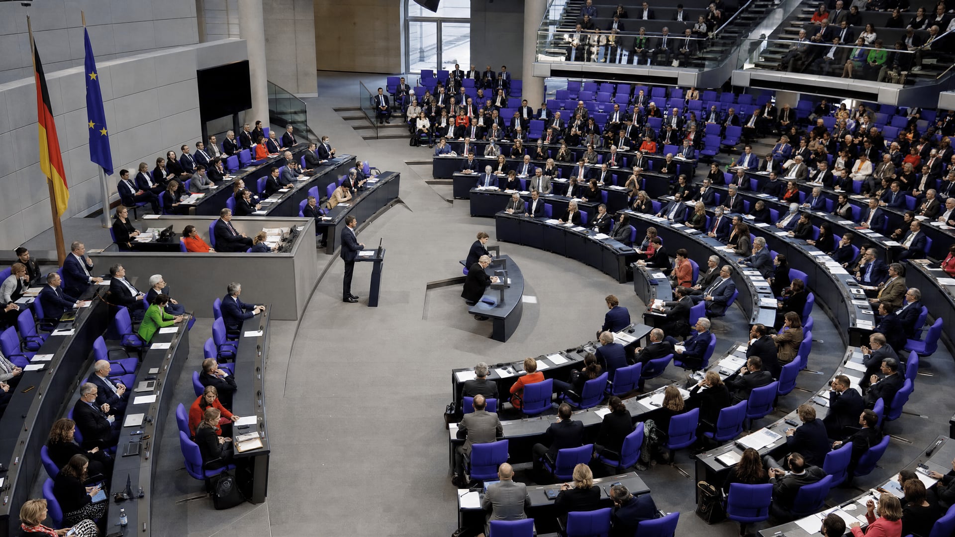 Bundestag chamber during a debate, with lawmakers seated and documents visible on desks.
